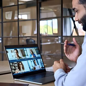 Image of a man sitting at a desk with a laptop and video camera, for remote work management.