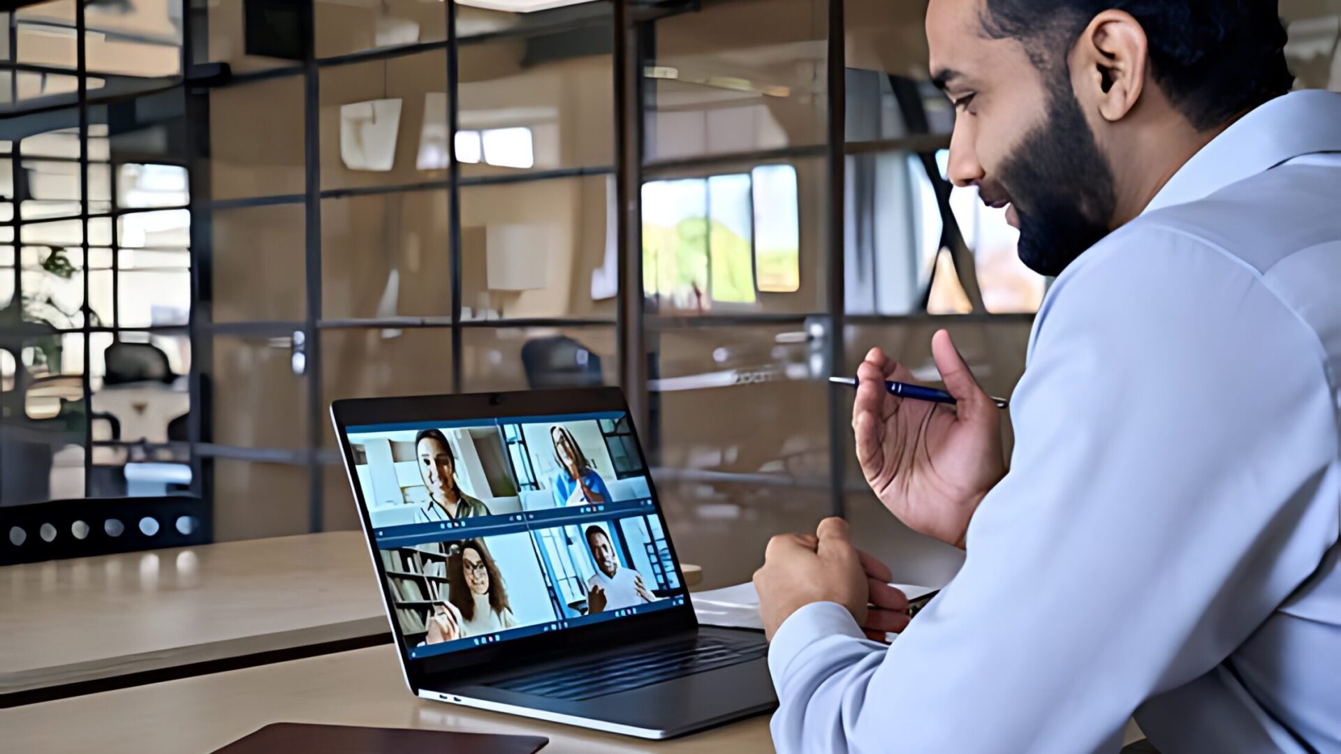 Image of a man sitting at a desk with a laptop and video camera, for remote work management.